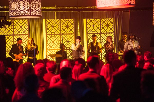 Band performing at indoor venue with red tinted glow of light on fans